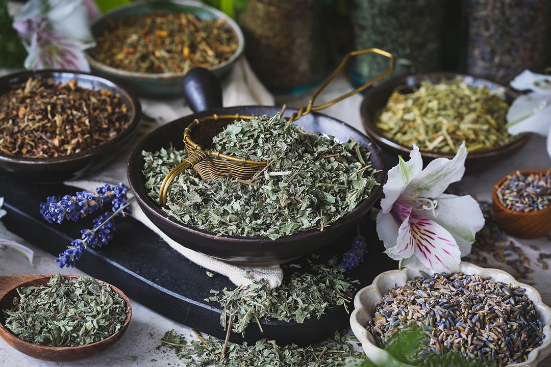 Bowls of colorful herbs surrounded by fresh flowers and an artful copper tea infuser. 